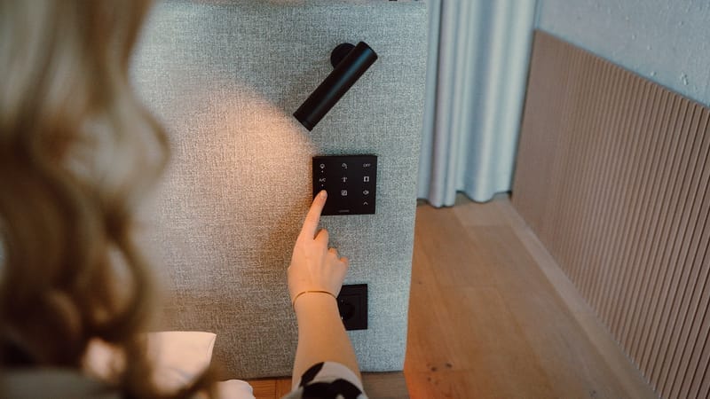 Czarny panel Loxone Touch Pure Flex z ikonami światła, klimatyzacji i rolet, wpuszczony w tapicerowany zagłówek