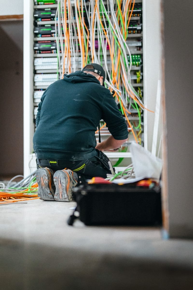 Elektryk podłączający przewody w wielorzędowej rozdzielnicy z modułami automatyki